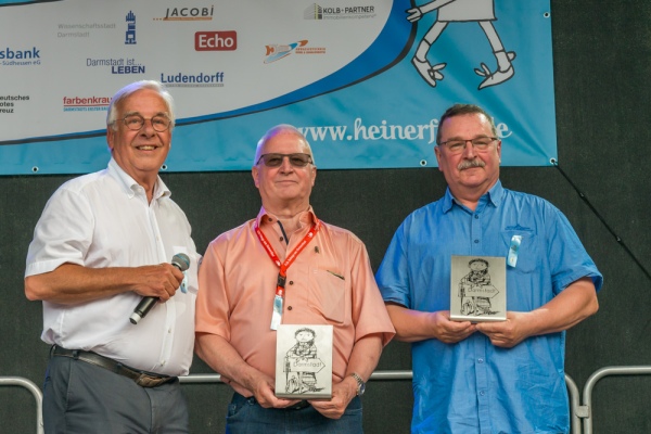 Wolfgang Koehler, Roland Dotzert und Peter Engels stehen nebeneinander auf der Herrngartenbühne, Dotzert und Engels halten die Trophäe für den Bekennenden Heiner in Händen